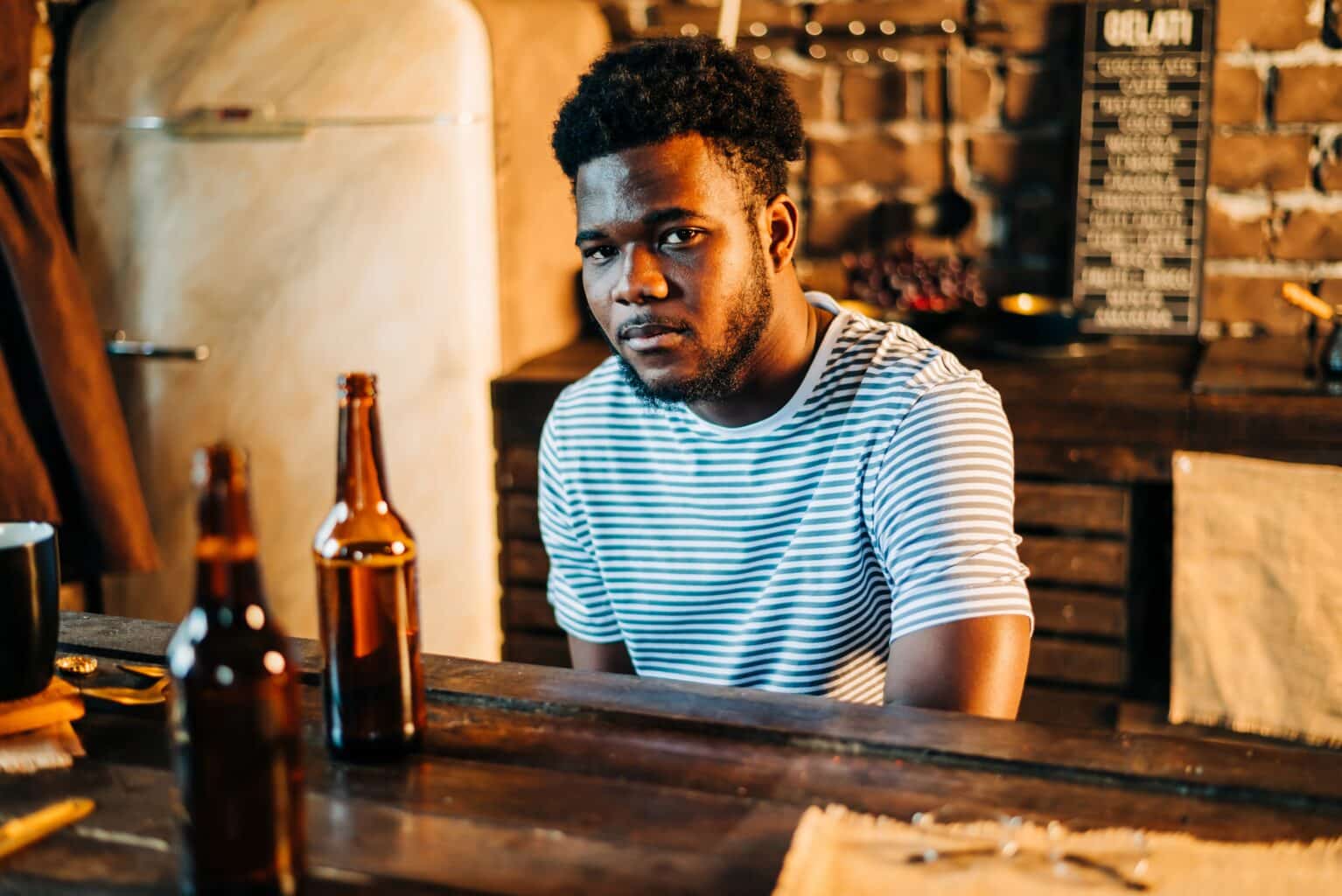 A young man suffering from depression and addiction looking sad while sitting in front of alcohol.